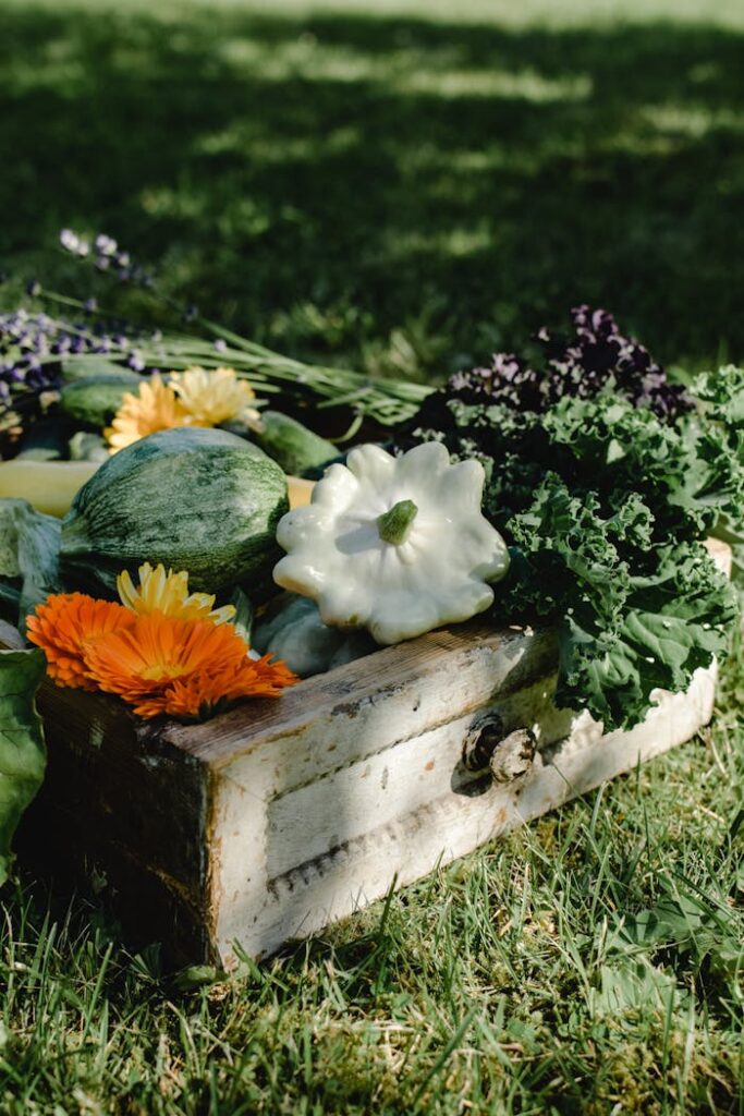 Vibrant collection of fresh organic vegetables and flowers in a rustic wooden box outdoors.